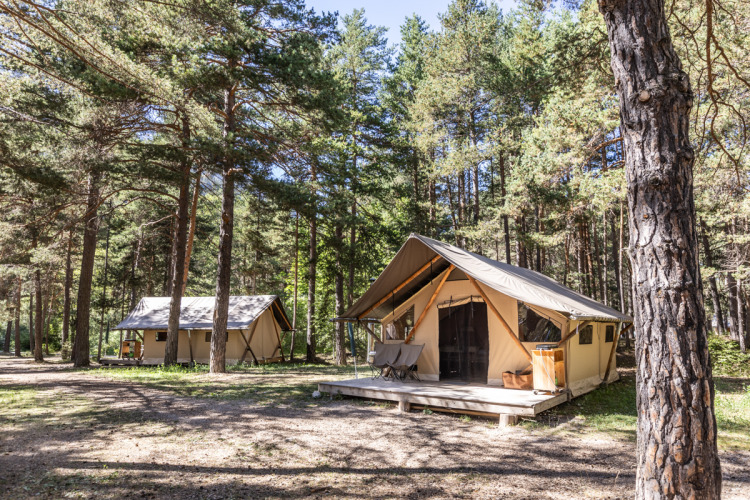 Safari Trappeur tents at Huttopia la Clarée in France, nestled in a sunlit forest clearing.