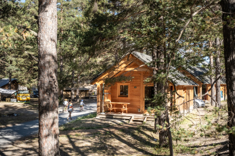 Vista del Chalet Montana Vista, una cabaña de madera entre árboles, personas caminando y coches estacionados.