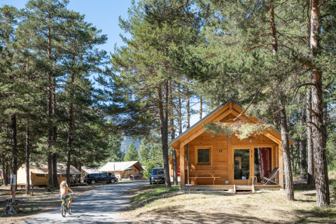 Træhytte Chalet Montana Vista i skoven ved Huttopia la Clarée, Frankrig, med cyklist og telte bagved.
