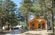 Chalet Montana Vista houten hut in Huttopia la Clarée, Frankrijk, omgeven door bomen en tenten, kind op fiets.