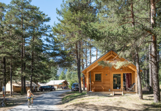 Træhytte Chalet Montana Vista i skoven ved Huttopia la Clarée, Frankrig, med cyklist og telte bagved.