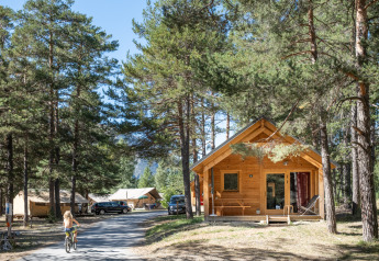 Chalet Montana Vista houten huisje bij Huttopia la Clarée, Frankrijk, tussen bomen en met een fietsend kind.