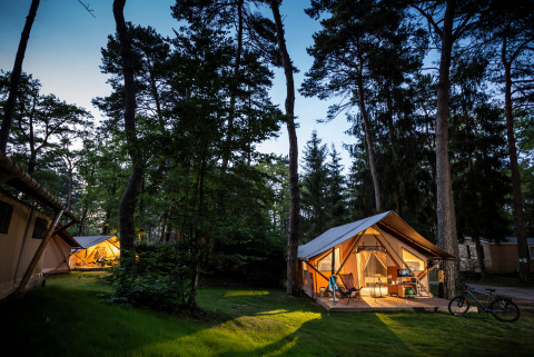 Vista nocturna de tiendas safari iluminadas en el bosque de Camping La Pinède - Excenevex en Francia.