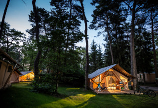 Vista nocturna de tiendas safari iluminadas en el bosque de Camping La Pinède - Excenevex en Francia.