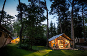 Vista serale di tende safari illuminate nella foresta al Camping La Pinède - Excenevex in Francia.