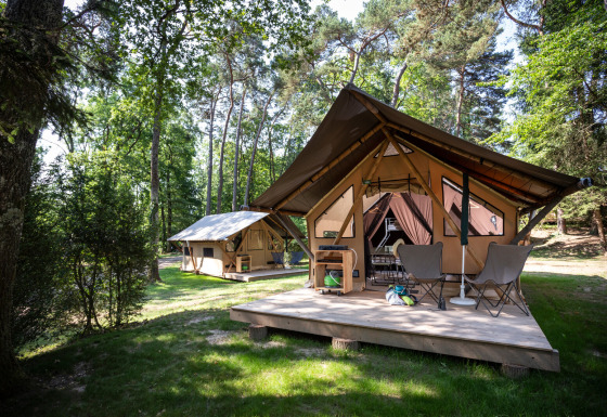 Safari-tent genaamd Canadienne Tent in het bos, met houten terras en campingstoelen aan de ingang.