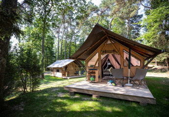 Safari-Zelt namens Canadienne Tent im Wald mit Holzterrasse und Campingstühlen vor dem Eingang.