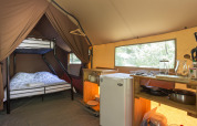 Interior de una tienda Canadienne en Camping La Pinède - Excenevex con literas, cocina y ventanal.