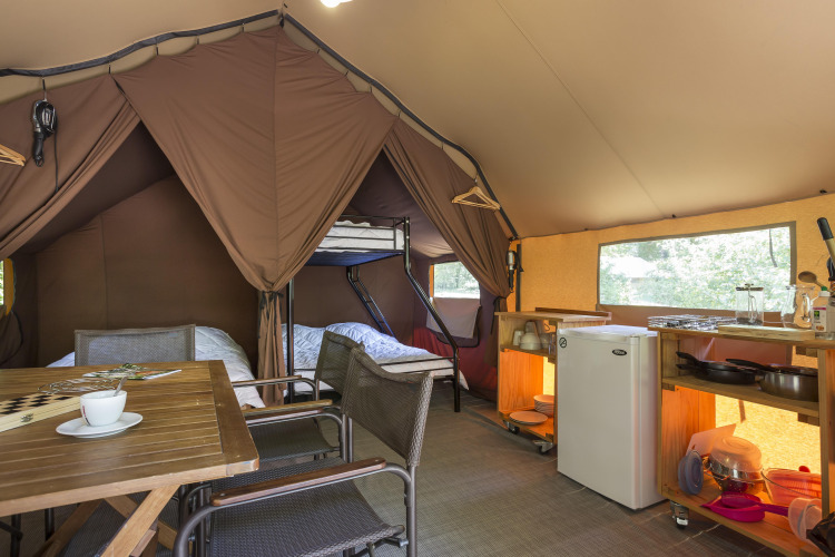 Interior de una tienda safari con cocina, mesa para comer y literas en Camping La Pinède, Francia.