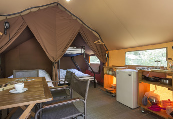 Interno di una tenda safari accogliente con angolo cottura, tavolo da pranzo e letti a castello a Camping La Pinède.