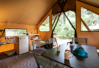 Binnenaanzicht van een safaritent met tafel, stoelen en keukentje op Camping La Pinède in Frankrijk.