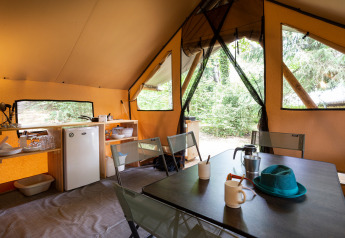 Vista interior de una tienda safari con mesa, sillas y cocina en Camping La Pinède en Francia.