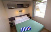 Gemütliches Schlafzimmer mit Doppelbett im Mobilheim auf Camping La Pinède in Excenevex, Frankreich.