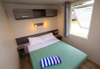 Acogedor dormitorio con cama doble en casa móvil de Camping La Pinède, Excenevex, Francia.