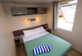 Gemütliches Schlafzimmer mit Doppelbett im Mobilheim auf Camping La Pinède in Excenevex, Frankreich.