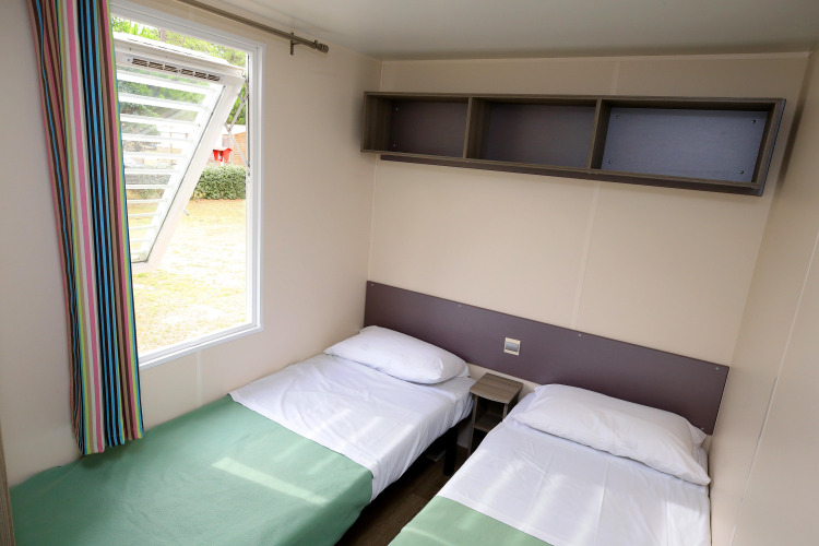 Dos camas individuales con sábanas blancas y una ventana abierta en mobile home de Camping La Pinède, Excenevex, Francia.