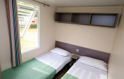 Due letti singoli con lenzuola bianche e finestra aperta in una casa mobile al Camping La Pinède, Excenevex, Francia.