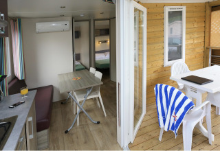 Vista interior y exterior de una casa móvil en Camping La Pinède - Excenevex, Francia, con comedor y terraza.