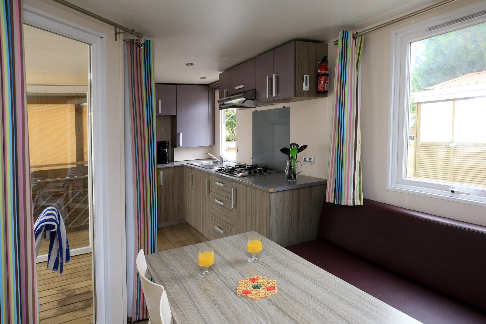 Keuken en eethoek van een stacaravan met gestreepte gordijnen op Camping La Pinède, Excenevex, Frankrijk.