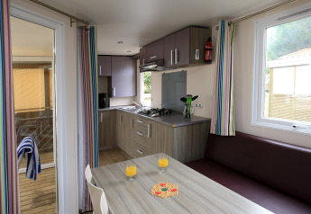 Cocina y comedor de una casa móvil con cortinas a rayas en Camping La Pinède, Excenevex, Francia.