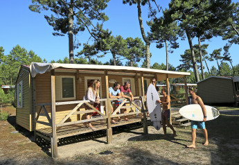 Grupo de jóvenes relajándose en una cabaña móvil, rodeados de árboles y dos con tablas de surf.