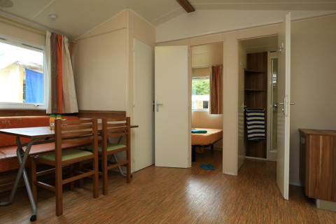 Interno di una casa mobile al Camping La Pinède di Excenevex, Francia, con zona pranzo e camera da letto.