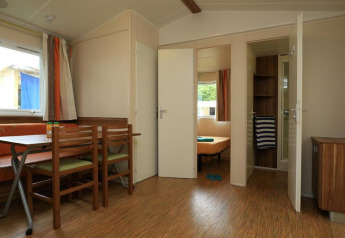 Intérieur d’un mobil-home au Camping La Pinède à Excenevex, France, avec coin repas et accès à la chambre.