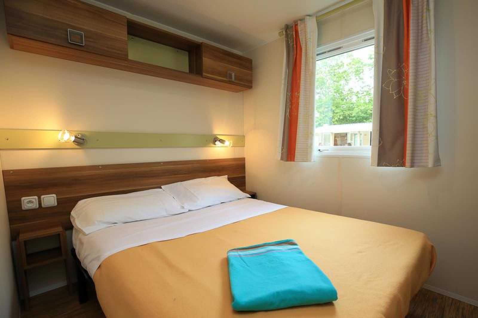 Slaapkamer in een stacaravan op Camping La Pinède, Excenevex, Frankrijk, met tweepersoonsbed en raam.