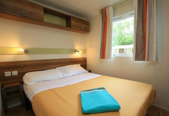 Slaapkamer in een stacaravan op Camping La Pinède, Excenevex, Frankrijk, met tweepersoonsbed en raam.