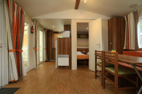 Vista interior de una casa móvil en Camping La Pinède, Excenevex, Francia, con sala, comedor y dormitorio.