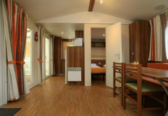 Interior view of a mobile home at Camping La Pinède, Excenevex, France, featuring dining and bedroom areas.