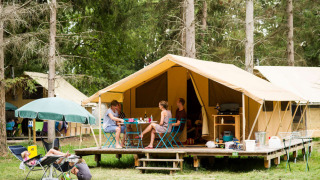 Gezin geniet buiten bij een Bungalow tent Classic safaritent op een camping tussen hoge bomen.