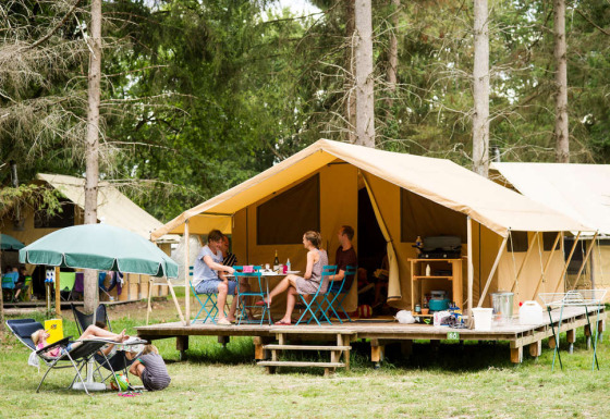 Familie hygger sig foran en Bungalow tent Classic safaritelt på campingplads, omgivet af skov.