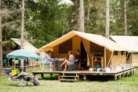 Family relaxing outside a Bungalow tent Classic safari tent on a campground, surrounded by tall trees.
