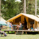 Familia disfruta al aire libre frente a una Bungalow tent Classic en un camping rodeado de árboles altos.