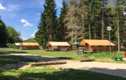 Safari bungalow tents at Huttopia Les Châteaux in France, surrounded by tall trees and grassy areas under blue sky.