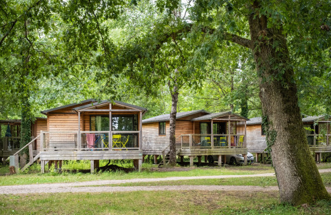 Chalet Evasion: houten chalets tussen bomen met terras en tuinmeubilair in een bosrijke omgeving.
