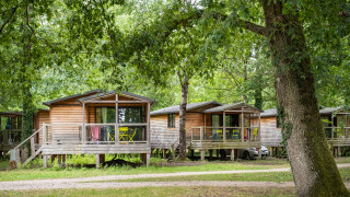 Chalet Evasion: houten chalets tussen bomen met terras en tuinmeubilair in een bosrijke omgeving.