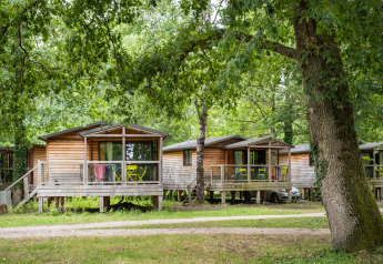 Træhytter ved navn Chalet Evasion blandt grønne træer med terrasser og havemøbler i skovområde.