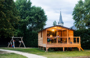 Chalet Evasion hut bij Huttopia Les Châteaux, Frankrijk, met kinderen op de schommel en familie op het terras.