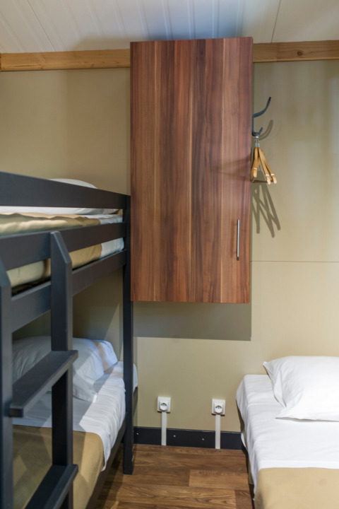 Interieur van Chalet Evasion bij Huttopia Les Châteaux, met stapelbed, eenpersoonsbed en houten kast.