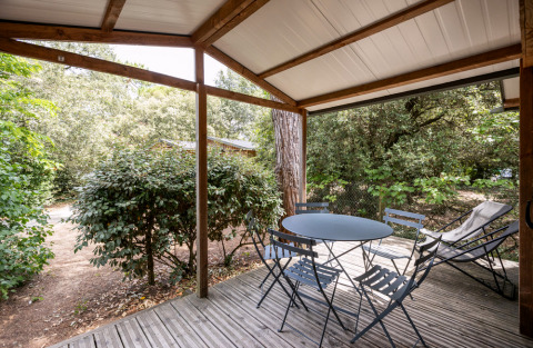 Terrasse couverte du Chalet Evasion à Huttopia Les Châteaux, avec table, chaises et vue sur la verdure