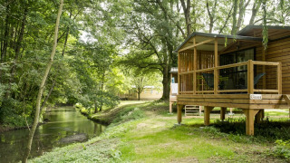 Houten chalet aan het water, Chalet Evasion Bord de Rivière, met terras en zicht op groene oever.