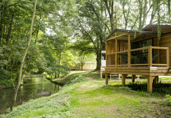 Wooden cabin by a river with a deck, Chalet Evasion Bord de Rivière, surrounded by lush green forest.