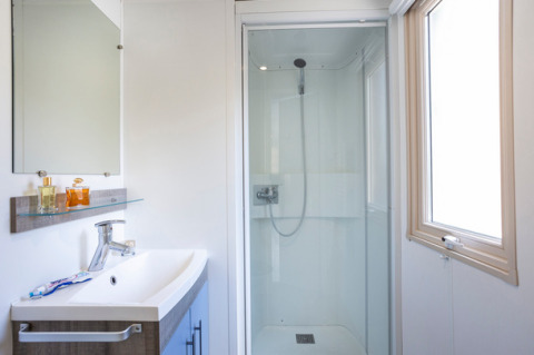 Modernes Badezimmer mit Dusche, Waschbecken und Spiegel in einem Mobile Home bei Huttopia Les Châteaux, Frankreich.