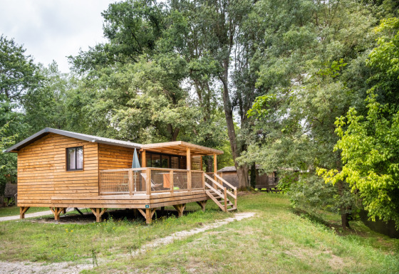 Cabaña Chalet Portland Riverside de madera, con terraza y rodeada de árboles verdes y naturaleza exuberante.