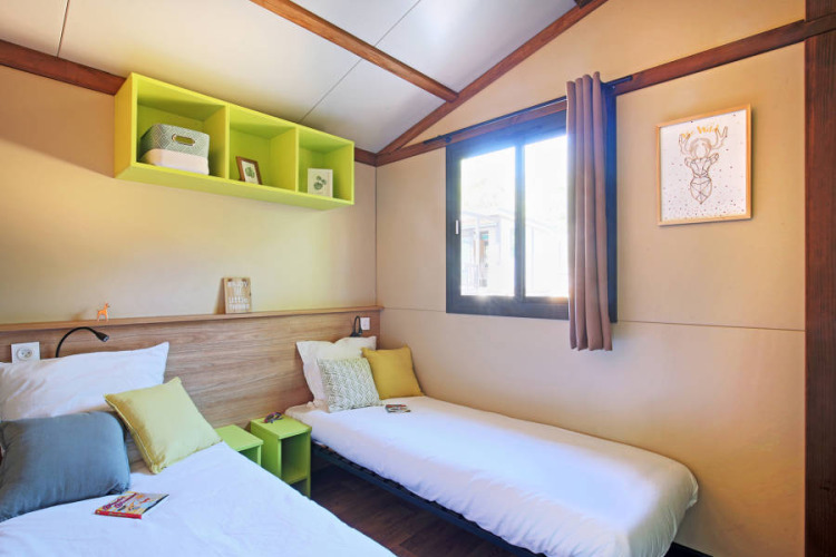 Acogedor dormitorio con dos camas individuales en Chalet Portland Riverside en Huttopia Les Châteaux, Francia.