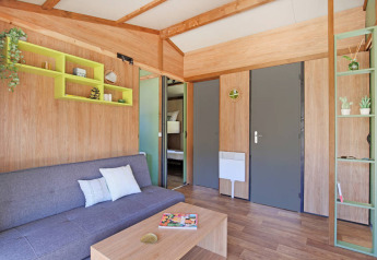 Moderne stue i Chalet Portland Riverside på Huttopia Les Châteaux, Frankrig med træ- og gråtoner.