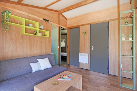 Sala de estar moderna en Chalet Portland Riverside en Huttopia Les Châteaux, Francia, con tonos madera y gris.