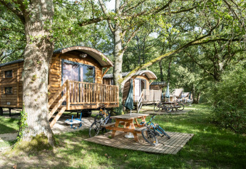 Holzhütten namens Roulotte im Wald mit Fahrrädern, Picknicktisch und viel grüner Natur im Sommer.